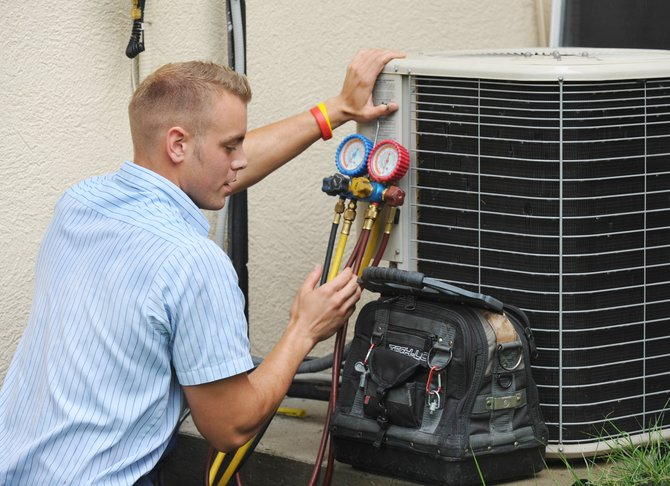 An HVAC service technician working on an air conditiner outside