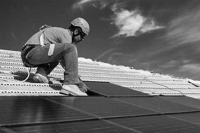 A man sitting on top of of a roof working on a solar panel who has undergone solar technician training