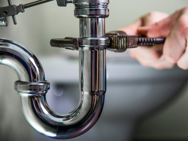 Plumber using a wrench to fix a pipe, illustrating workforce development in plumbing