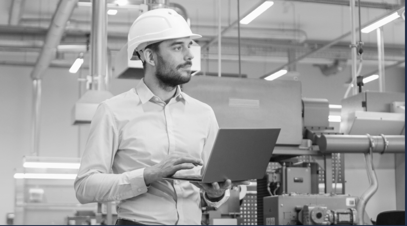A skilled trade worker in a hard hat holding a laptop