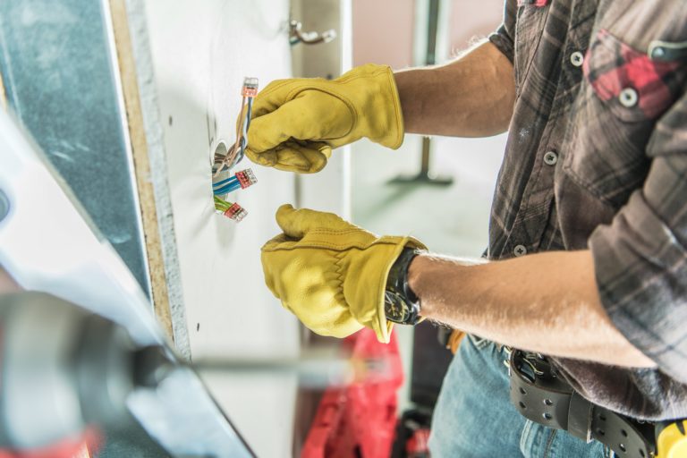 An electrician in a plaid shirt and yellow gloves fixing wires