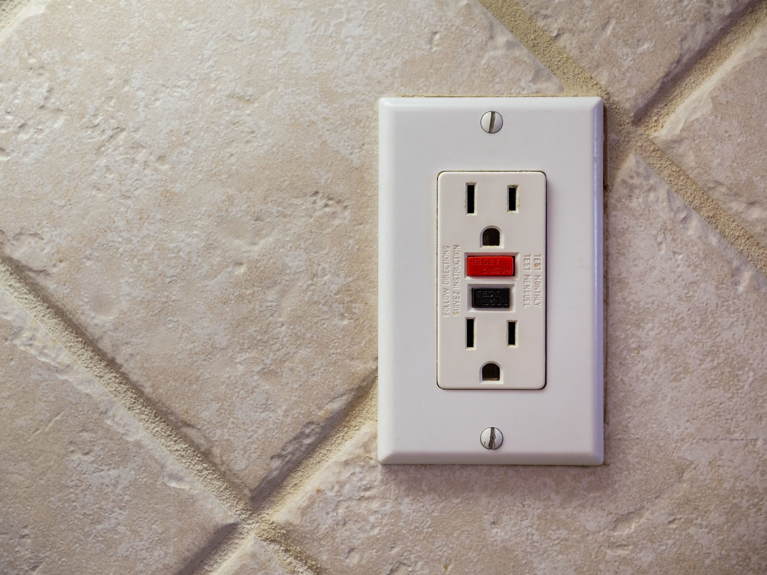 A white electrical outlet on a tiled wall