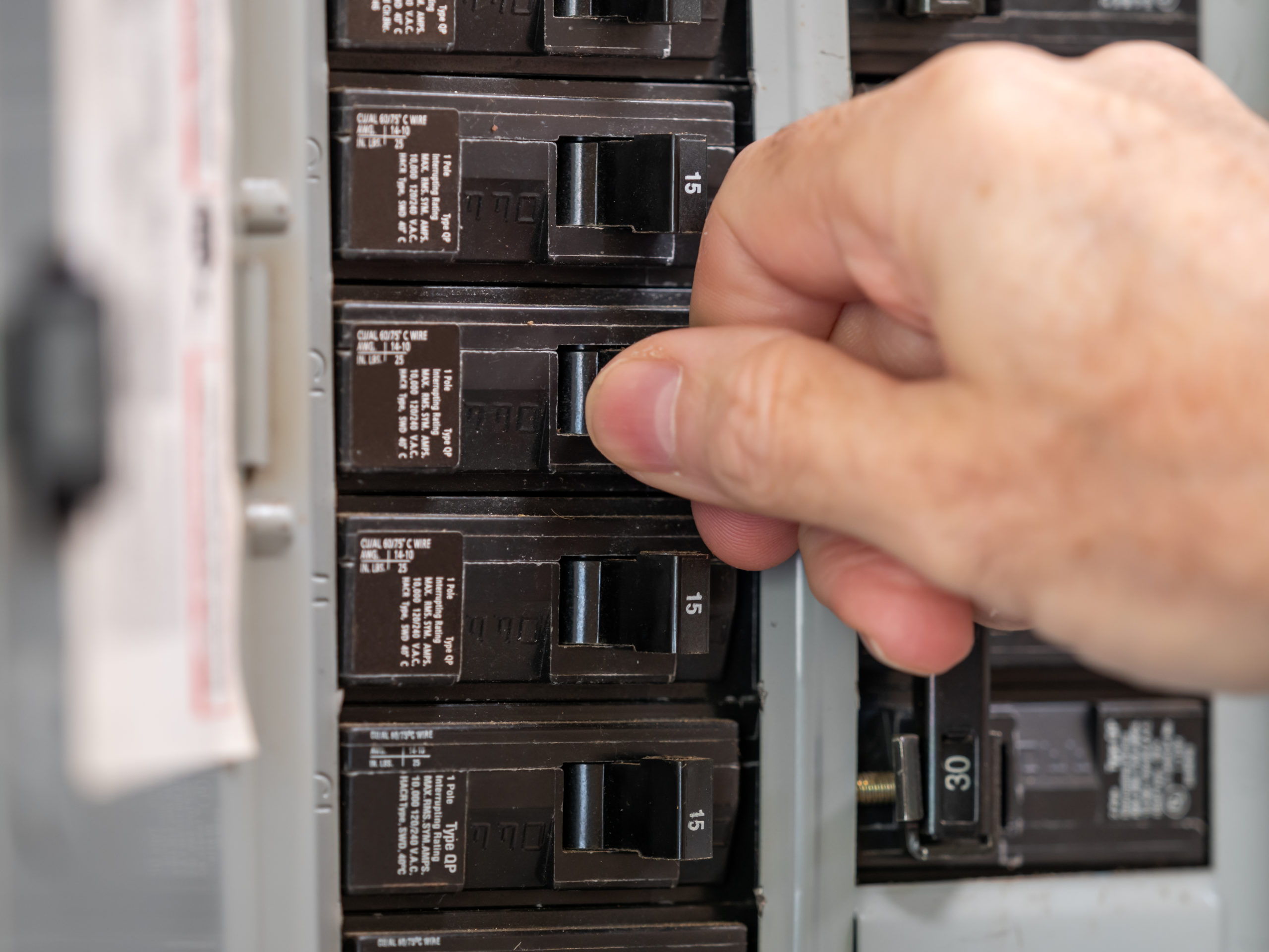 A hand is pressing a button on a circuit breaker