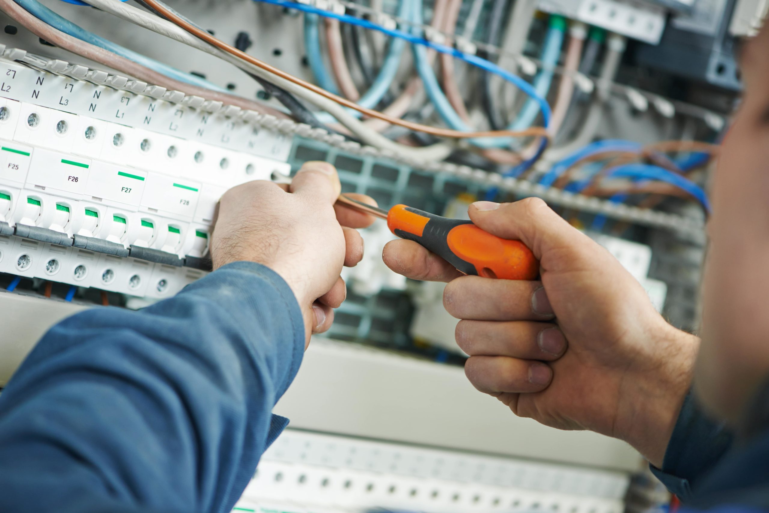 An electrician using a screwdriver to work on a electrical panel