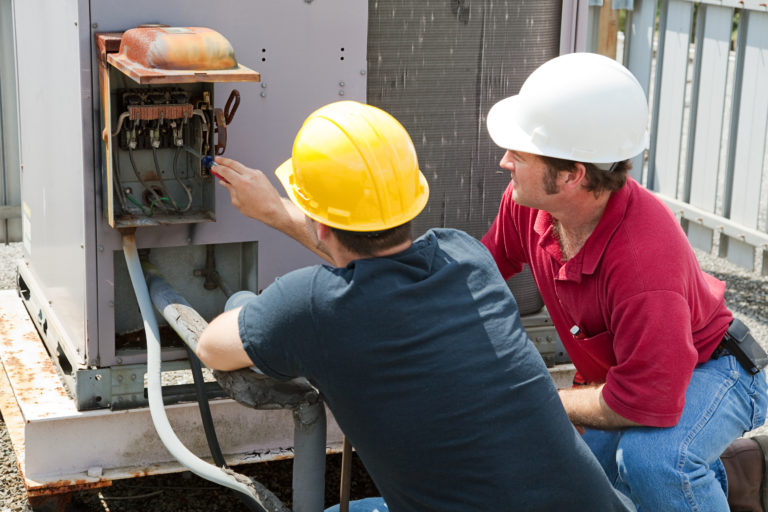 Two men in hard hats working on an air conditioner