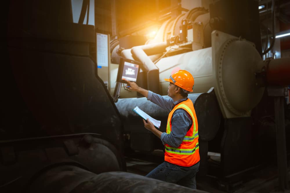 A man with an orange vest inspecting a commercial HVAC unit demonstrating knowledge from online skilled trades courses