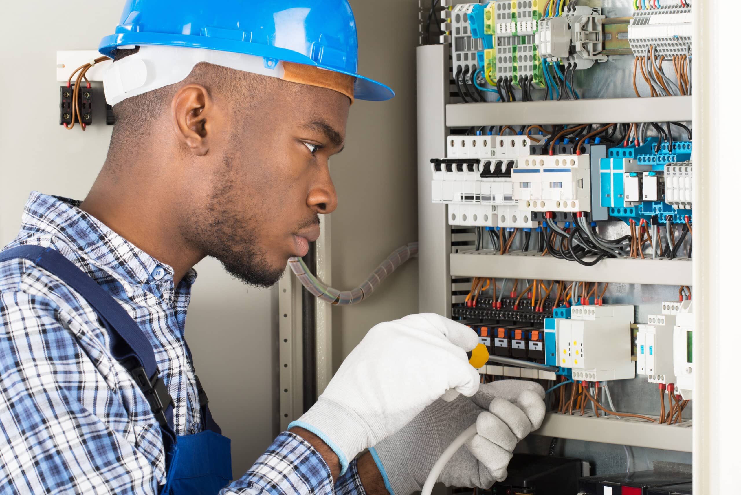 An apprentice in a hard hat working on an electrical panel