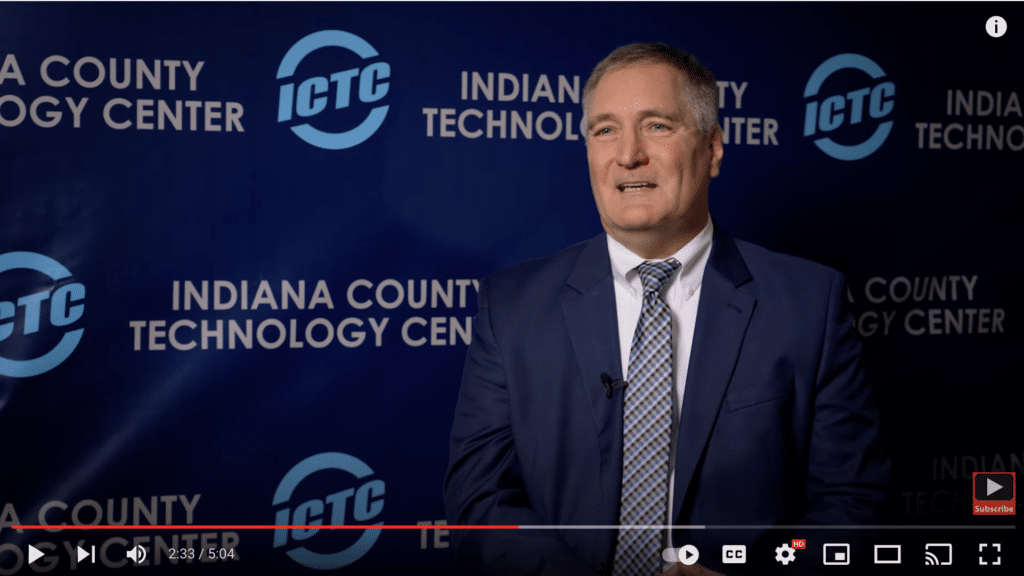 A man in suit and tie infront of a display that says Indiana County Technology Center