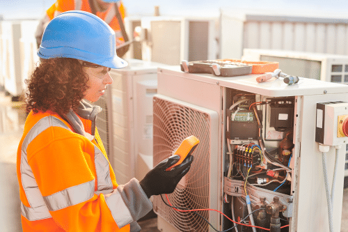 A woman in an orange safety vest is checking the temperature of an air conditioner who has undergone a workforce development program
