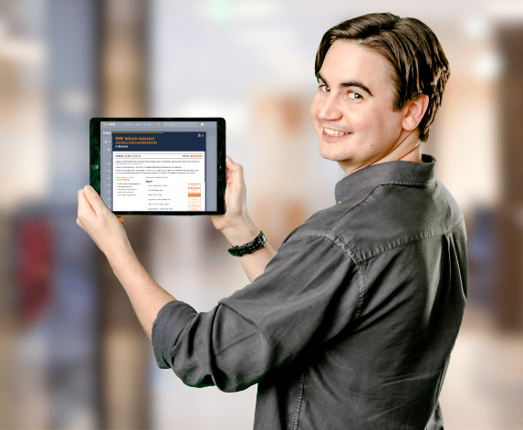 A man in a grey shirt holding a tablet and showing the Skillmill application for skilled trades training
