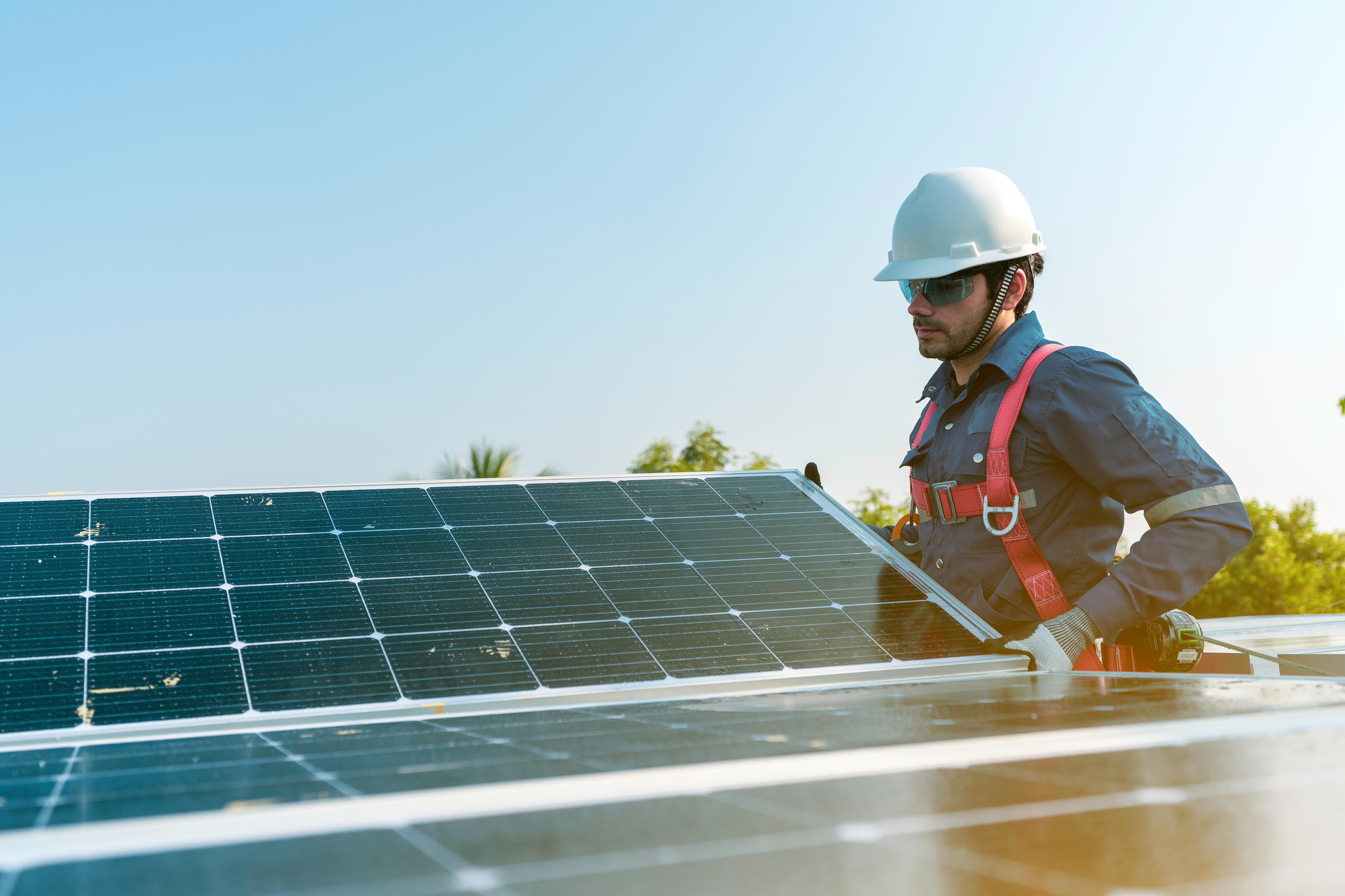 A man in a hard hat and safety vest working on a solar panel