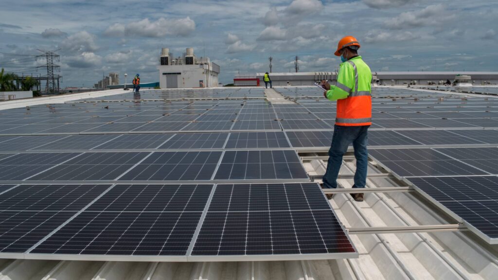 A man in an apprenticeship for large scale solar standing on a roof with a bunch of solar panels