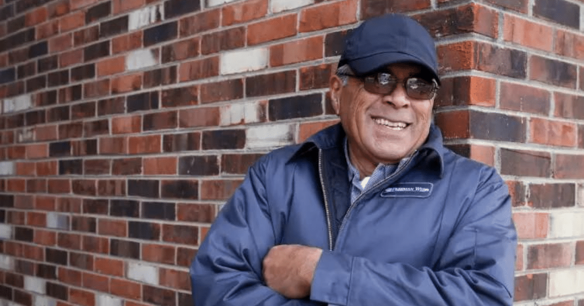 a man in a blue jacket leaning against a brick wall