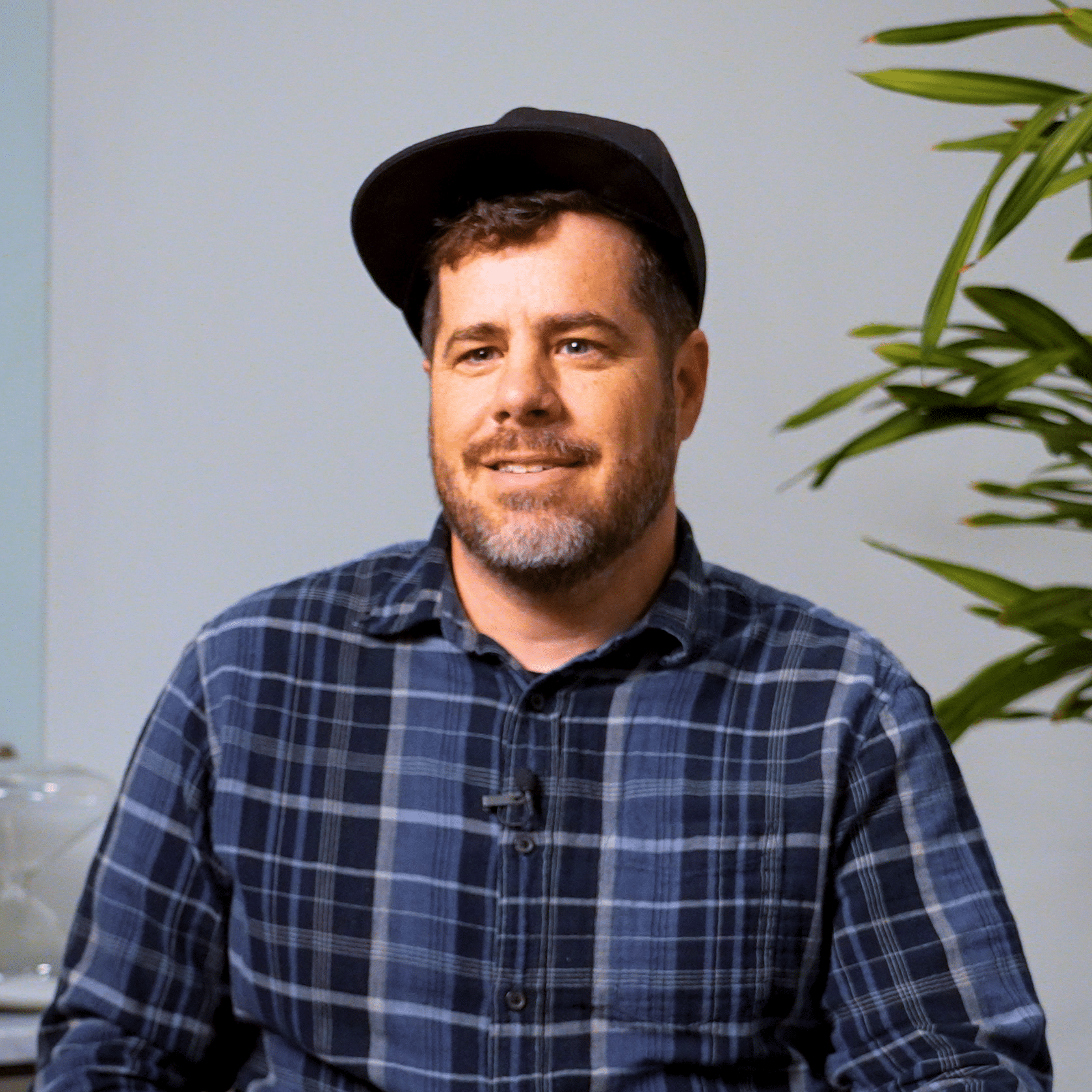a man with a hat sitting in front of a plant
