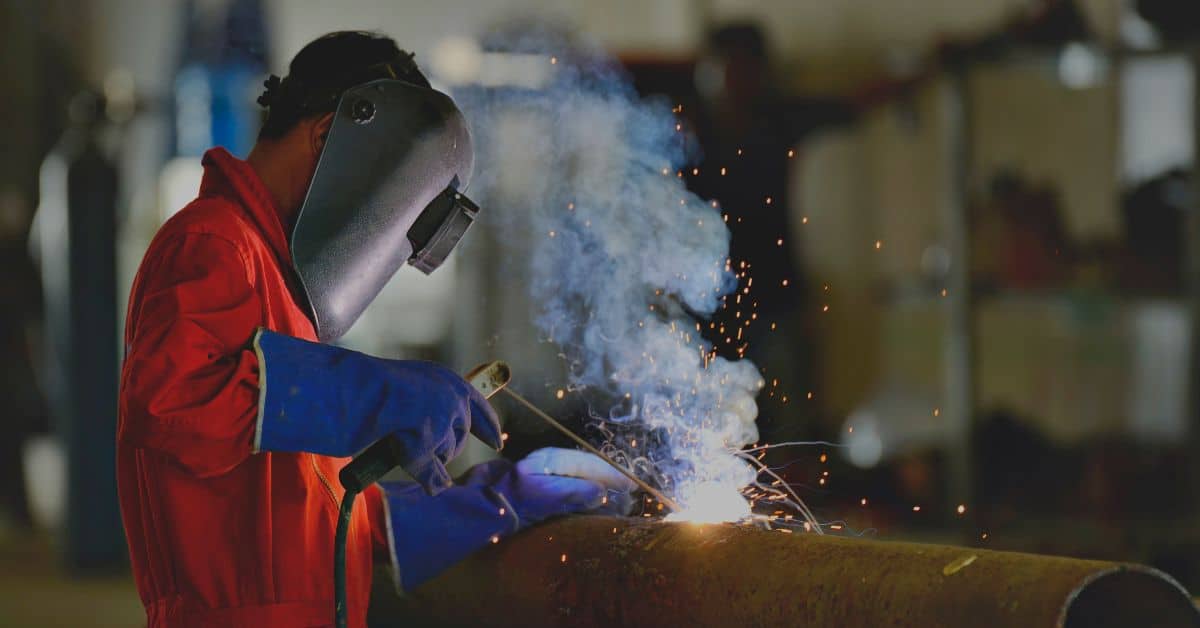 a man in a red jacket welding a pipe